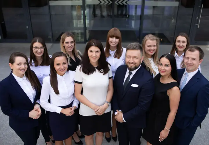 Grupa prawników i radców prawnych w garniturach i eleganckich strojach stoi przed budynkiem.