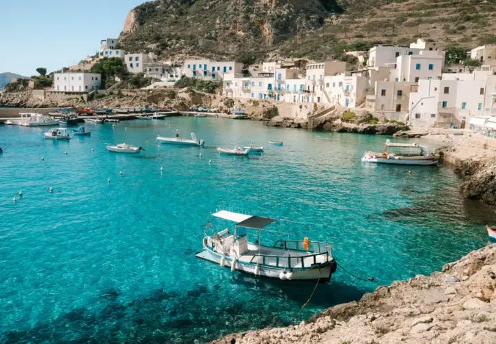 A picturesque harbor with white buildings and boats, showcasing one of the top places to see in Sicily.
