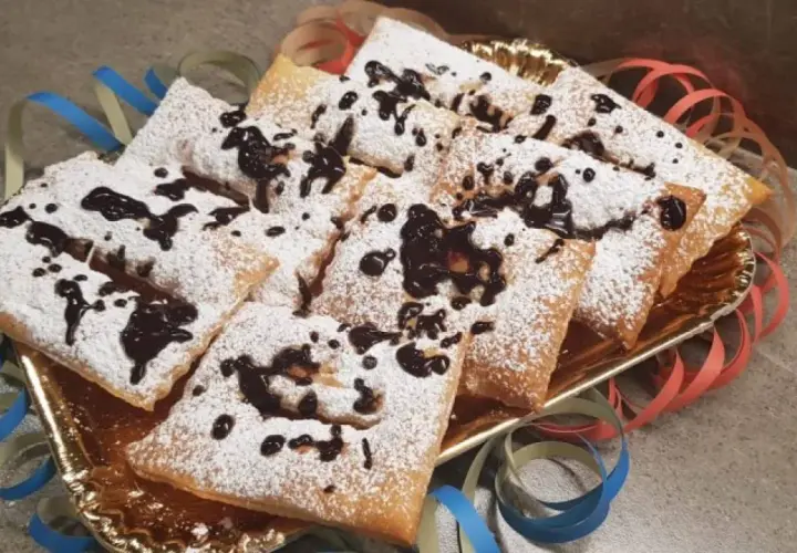 Chiacchiere morbide cosparse di zucchero a velo e gocce di cioccolato, pronte per festeggiare il Carnevale.
