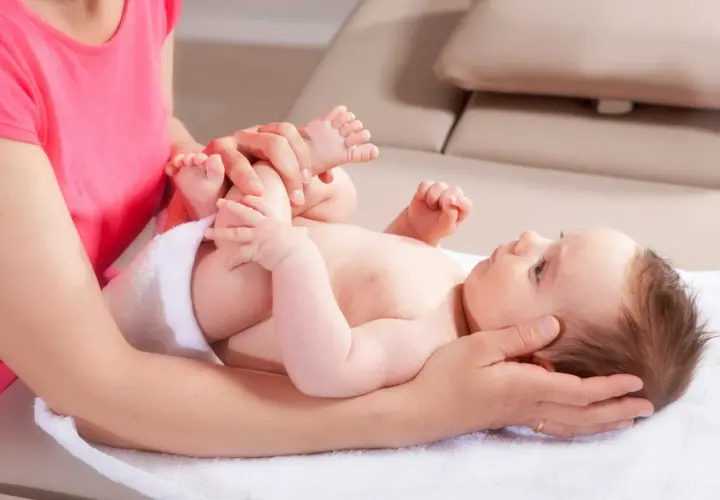Sanfte Hände untersuchen die Füße eines Babys. Eine Mutter fragt sich, wann mit Baby zum Osteopathen gehen sollte, um solche Behandlungen zu erhalten.