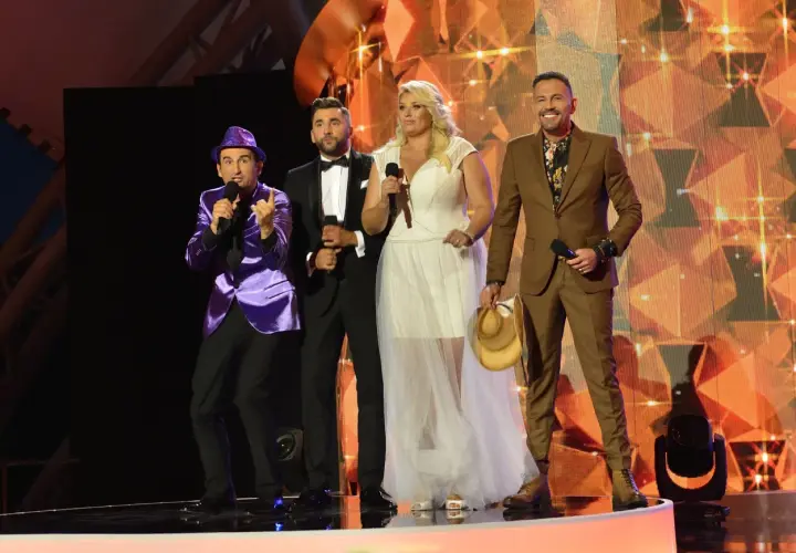 Na scenie festiwalu weselnych przebojów Mrągowo: prowadzący w fioletowej marynarce, panowie w garniturach i kobieta w białej sukni.
