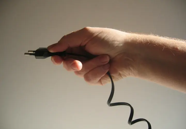 Dłoń trzymająca czarny kabel z wtyczką.