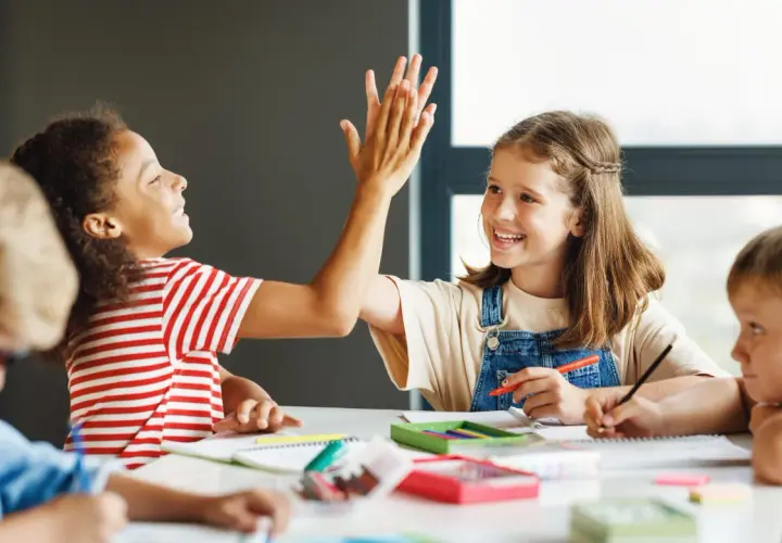 Kinder geben sich High-Five, während sie konzentriert arbeiten. Dieses Bild zeigt eigenverantwortliches Arbeiten und Freude am Lernen.