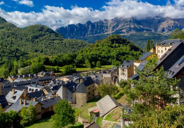 Pueblos del Pirineo Catalán, con tejados oscuros y montañas verdes de fondo bajo un cielo azul con nubes.