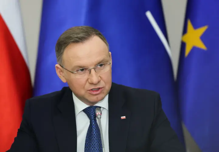 Andrzej Duda w garniturze, za nim flagi Polski i UE. Prawdziwe powody dla których Andrzej Duda zapowiedział serię wet do ustaw budżetowych.