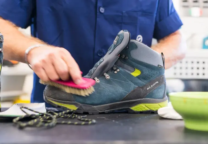 A person is cleaning a hiking boot with a brush, demonstrating how to maintain shoes.