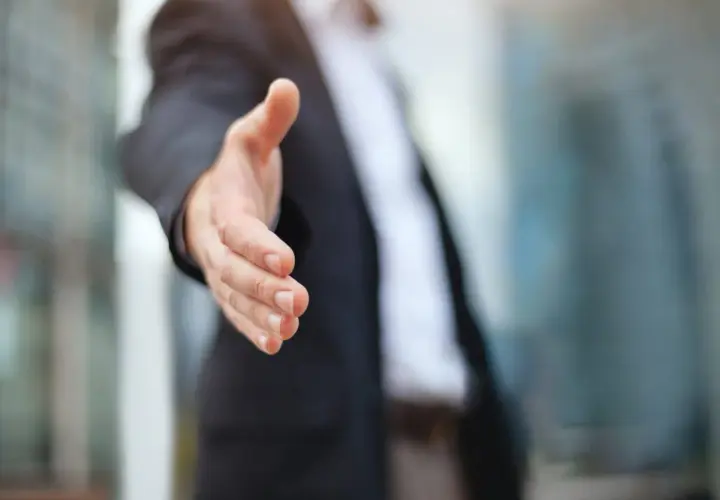 Biznesmen wyciąga rękę do uścisku, symbolizując partnerstwo i współpracę. Dowiedz się, jak założyć spółkę cywilną.