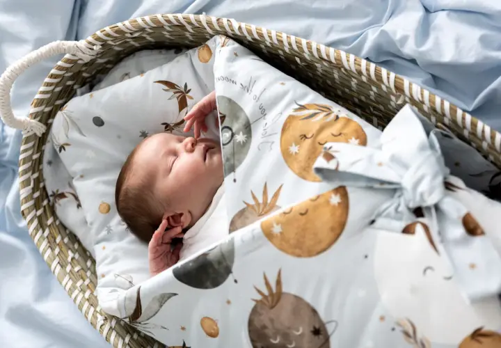 Śpiące dziecko otulone rożkiem niemowlęcym z motywem księżyców i gwiazdek. Idealny wybór dla maluszka.