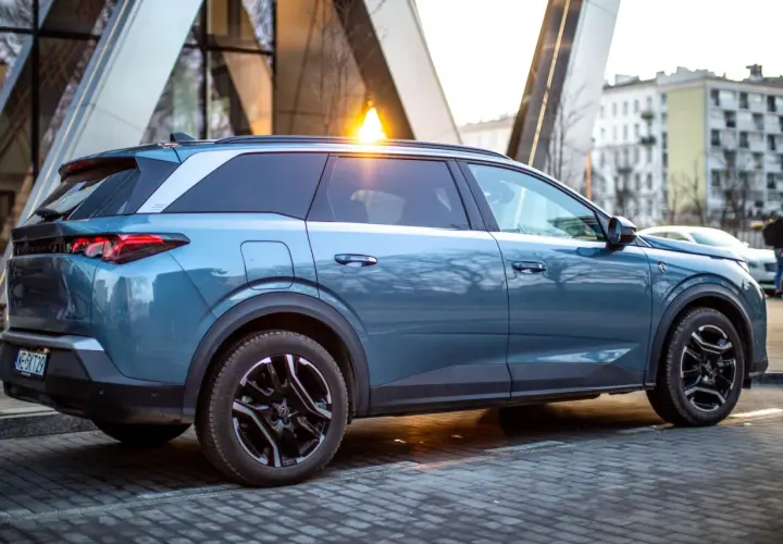 Niebieski Peugeot 5008 na tle nowoczesnej architektury. Wiele osób szuka peugeot 5008 opinie przed zakupem.