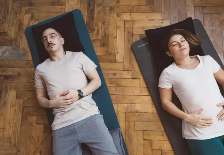 Un couple pratique la respiration profonde technique sur des tapis de yoga. Ils sont allongés sur le dos, les yeux fermés, les mains sur le ventre.