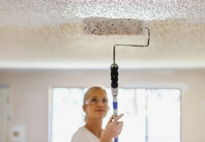 Donna imbianca il soffitto con un rullo, un modo semplice per rinnovare casa.