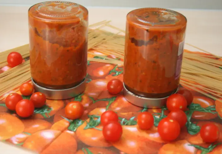 Zwei Gläser mit hausgemachtem tomaten sugo stehen neben Spaghetti. Frische Kirschtomaten zieren die Serviette mit Tomatenmuster.