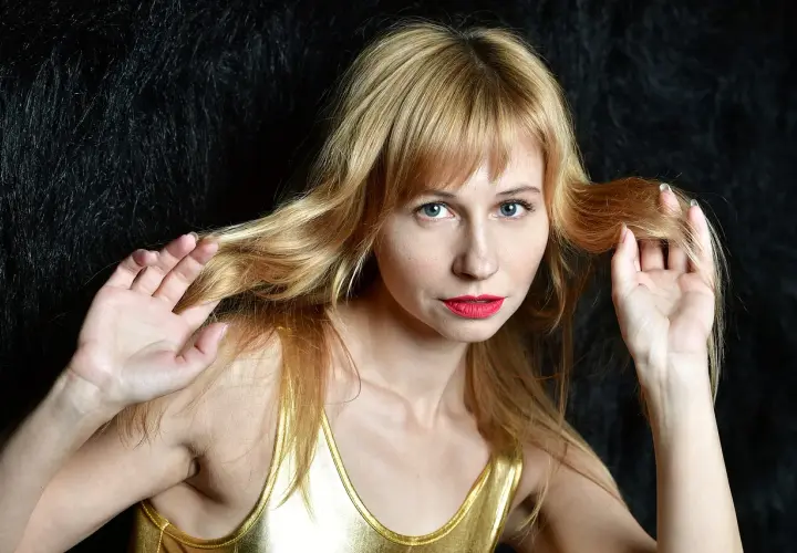 Kobieta z blond grzywką i niebieskimi oczami, zastanawiająca się, ile rośnie grzywka w tydzień.