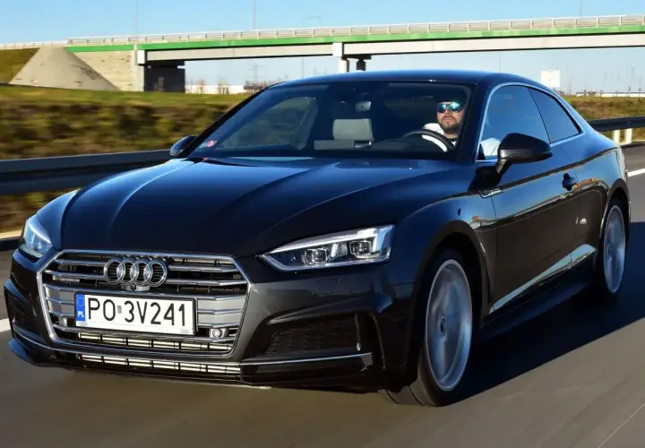 Czarny Audi A5 2025 z kierowcą w okularach przeciwsłonecznych jedzie po autostradzie.