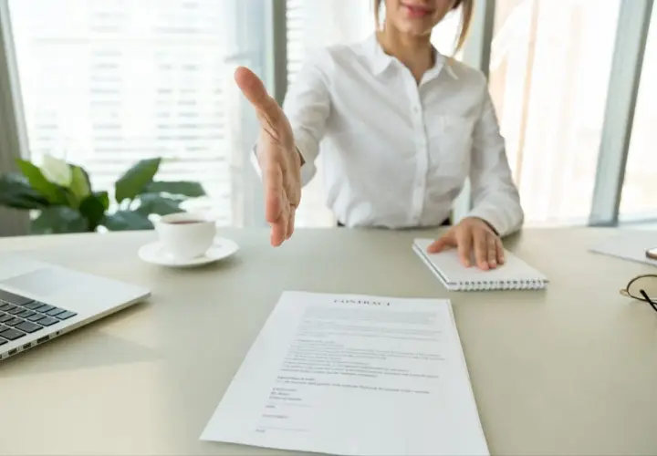 Bizneswoman wyciąga rękę do uścisku nad dokumentem "CONTRACT". Może to być umowa, wykreślenie hipoteki lub inny ważny wpis.