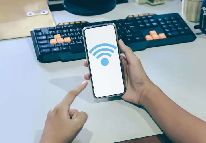 Dłoń trzyma smartfon z ikoną Wi-Fi. Dowiedz się, jak sprawdzić częstotliwość Wi-Fi w telefonie, aby zoptymalizować połączenie.
