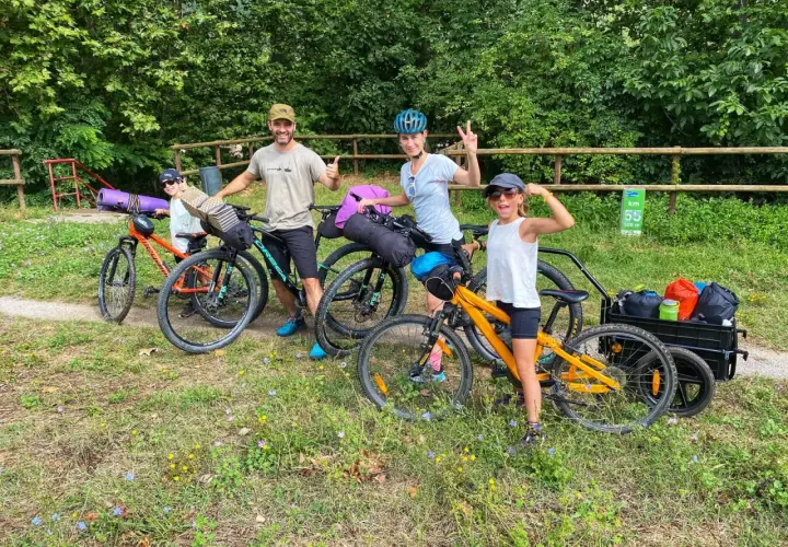 Familia lista para la ruta Pirinexus, con bicicletas y equipaje, disfrutando del paisaje verde.