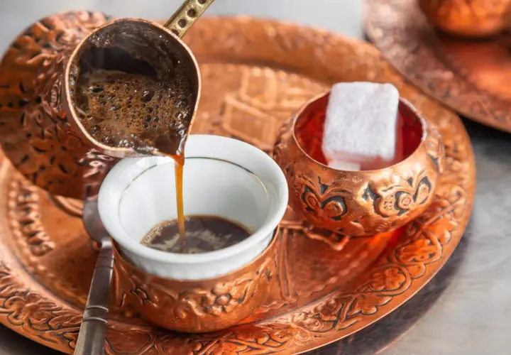 Frisch aufgebrühter, bester türkischer Kaffee fließt aus einer Kupferkanne in eine kleine Tasse. Daneben liegen süße Loukoum-Würfel.