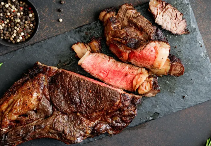 Un steak de bœuf juteux, coupé en tranches, révèle une cuisson parfaite grâce à la méthode de cuisson reverse sear. Poivre noir et blanc en accompagnement.