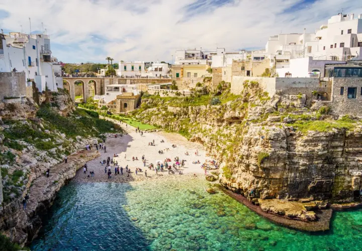Malownicze klify i białe domy Polignano a Mare, z plażą pełną ludzi i turkusową wodą.