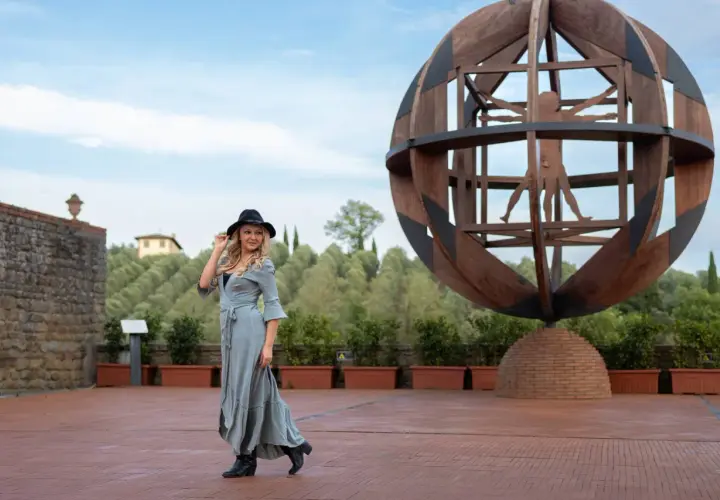 Donna con cappello nero e abito lungo in un'area panoramica del vinci centro storico, con la scultura dell'Uomo Vitruviano sullo sfondo.
