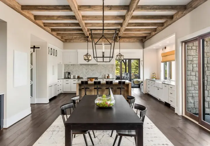 Comedor y cocina de estilo farmhouse con vigas de madera expuestas, isla central con taburetes y mesa oscura.