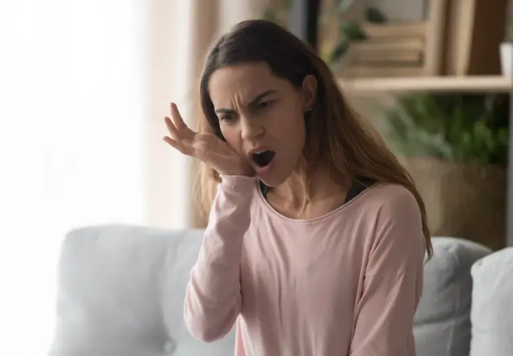 Donna con espressione sofferente, si tocca la guancia, manifestando un forte dolore diffuso a tutti i denti.