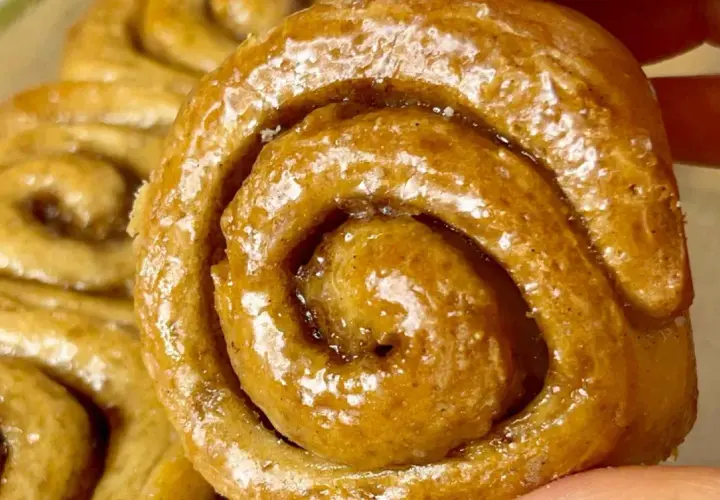 Un primo piano di soffici cinnamon rolls glassati, con la loro spirale invitante e il profumo di cannella che sembra quasi percepibile.