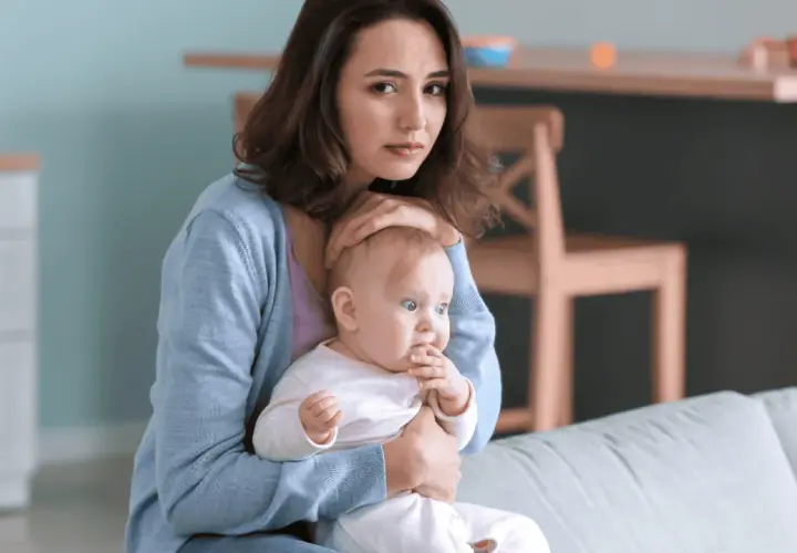 Smutna młoda mama tuli dziecko, czując się przytłoczona. To może być depresja w ciąży, która dotyka wiele kobiet.