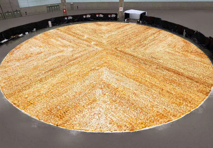 Gigantyczna pizza, największa na świecie, rozłożona na ogromnej przestrzeni. Jej złocisty kolor i równomierne posypanie przyprawami zachwycają.