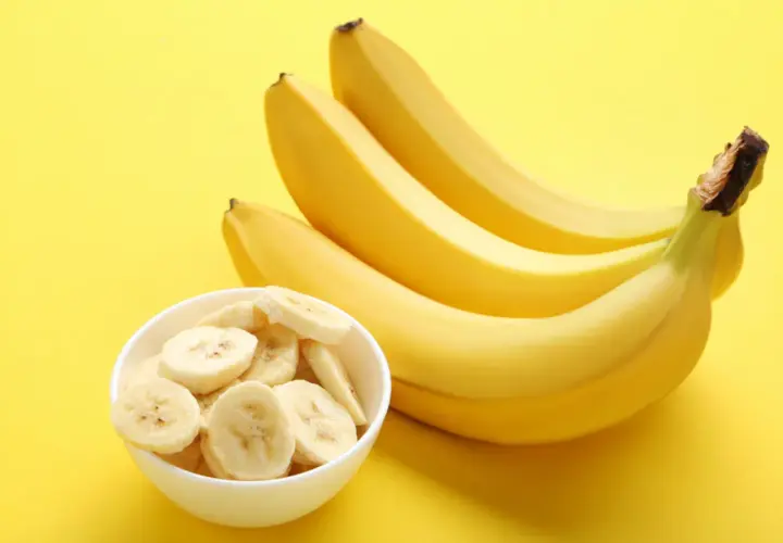 Pytanie: czy banany są kaloryczne? Na żółtym tle pęczek żółtych bananów i miseczka z plasterkami banana.