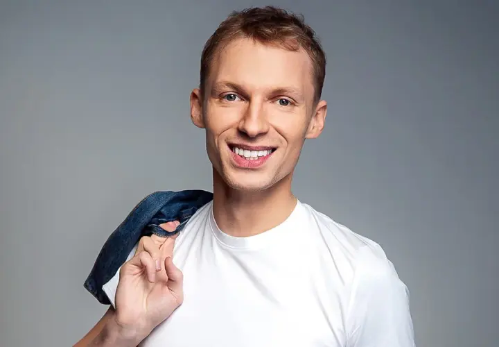 Uśmiechnięty Igor Herbut w białej koszulce z dżinsową kurtką na ramieniu.