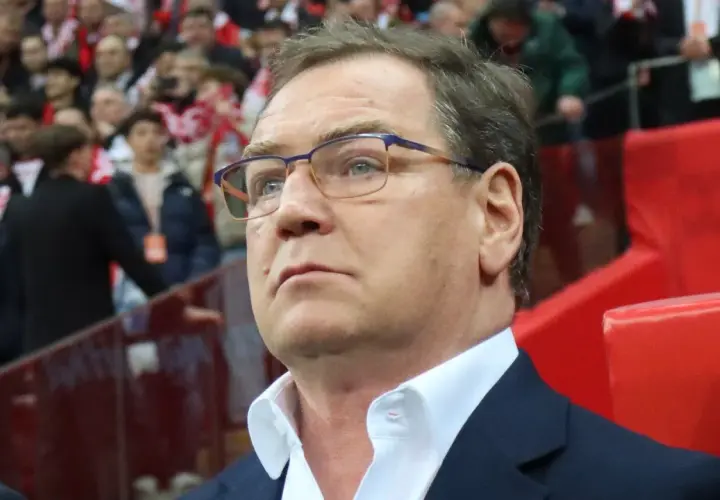 Trener w okularach z uwagą obserwuje trybuny, być może analizując potencjalnych kandydatów do reprezentacji.