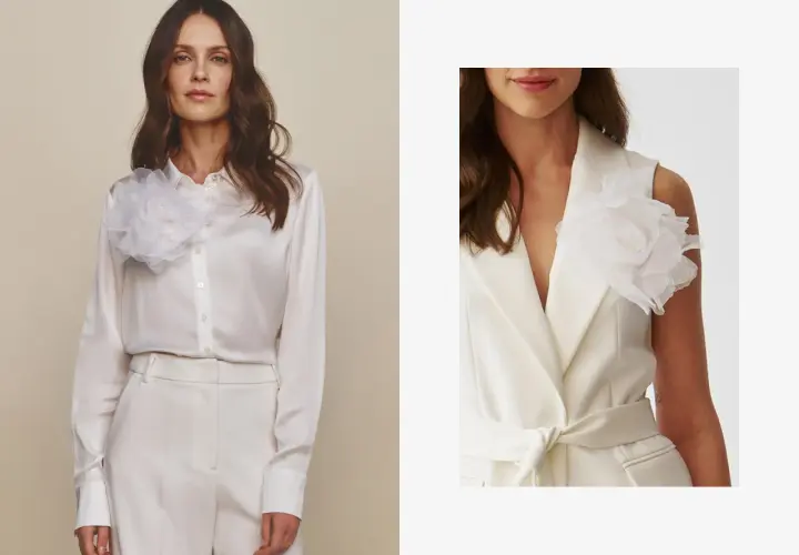 Elegancka kobieta w białej satynowej koszuli i marynarce bez rękawów, obie ozdobione białą broszką w kształcie kwiatu. Inspiracja, jak nosić broszki.