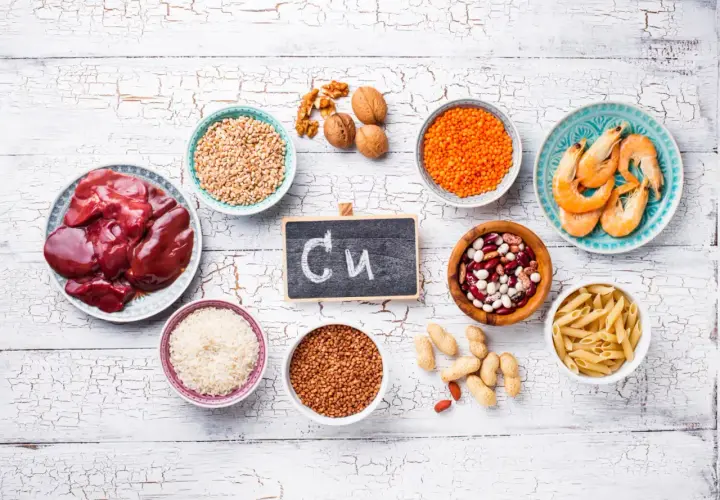 Na tabliczce napisano "Cu". Wokół niej są produkty bogate w miedź: wątróbka, soczewica, fasola, orzechy, krewetki, ryż, kasza gryczana, pszenica, makaron i orzeszki ziemne. Czy miedź rdzewieje? Nie, ale jest niezbędna dla zdrowia.