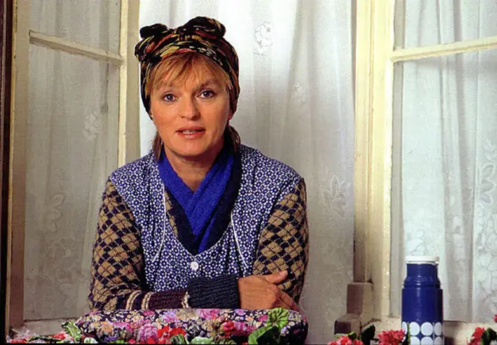 Else Stratmann sitzt am Fenster, eine bunte Kopftuch ziert ihr Haar. Sie trägt eine blaue Bluse mit weißen Punkten und eine Strickjacke.