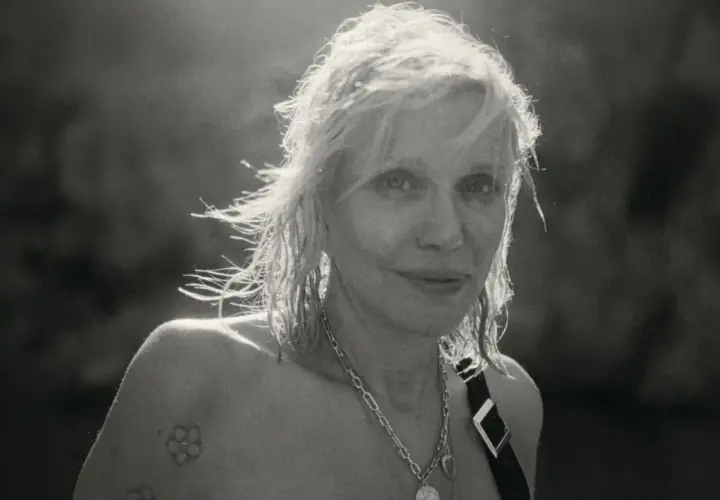 Courtney Love, ikona grunge, z rozwianymi włosami i tatuażem na ramieniu, emanuje siłą.