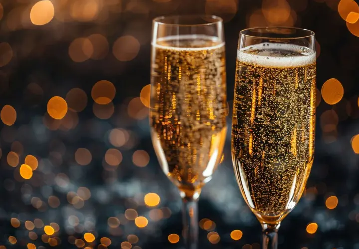 Dwa kieliszki musującego prosecco, które często mylone jest z szampanem, na tle rozmytych, złotych świateł.