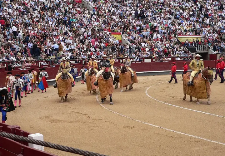 Inicio de que es una corrida de toros: picadores a caballo con caparazones, toreros y público en las gradas.