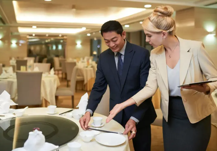 Ein Mann und eine Frau richten einen Tisch in einem Restaurant für ein Event her. Sie besprechen Details, die für das eventmanager gehalt wichtig sind.