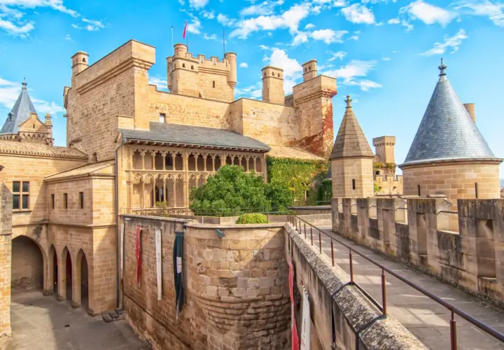 Imponente fortaleza de los castillos de España, con torres cónicas y un patio bajo un cielo azul y nubes blancas.