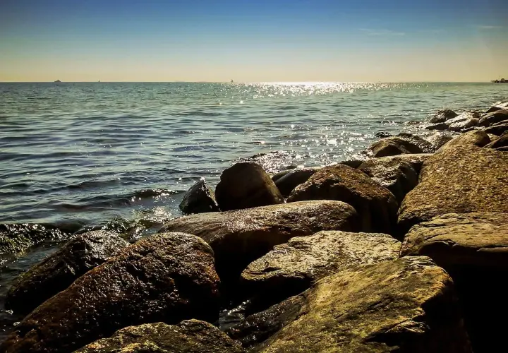 Kamienista plaża, fale rozbijające się o brzeg. W oddali widać statki i horyzont. Idealne miejsce na spacer w miejscowościach obok Ustki.