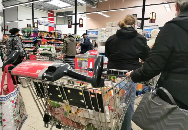 Ludzie robią zakupy w supermarkecie, zastanawiając się, czy w Wielką Sobotę można pracować. Wózek sklepowy pełen produktów.
