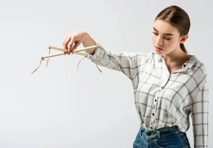Kobieta trzyma drewniany krzyżak marionetki, ukazując słabe punkty manipulatora.
