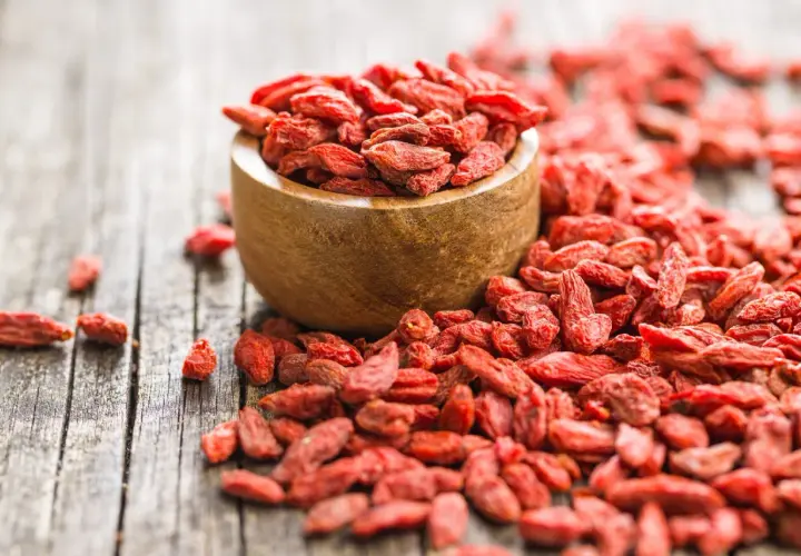 Suszone jagody goji rozsypane wokół drewnianej miseczki. Idealne do deserów, smoothie i jako zdrowa przekąska.