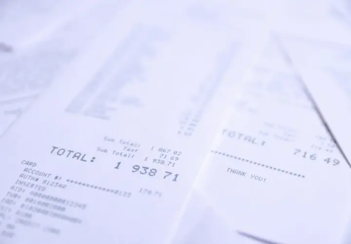 Stosy paragonów z widocznym napisem "TOTAL". Jeden z nich pokazuje kwotę 1 938,71, inny 716,49. Wsto oss.