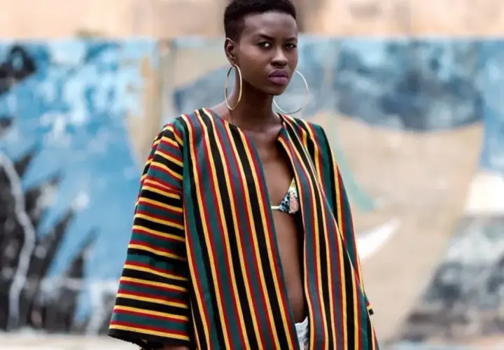 A woman models a vibrant Ankara fabric jacket with bold stripes of red, yellow, green, and black.
