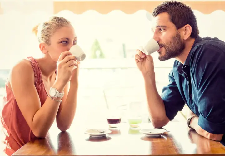 Coppia al bar, lui la guarda intensamente, un uomo innamorato in segreto che cerca il suo sguardo mentre bevono un caffè.