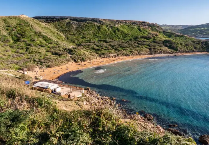 Malta's Riviera Beach: piaszczysta plaża, turkusowa woda i zielone wzgórza tworzą idylliczny krajobraz.