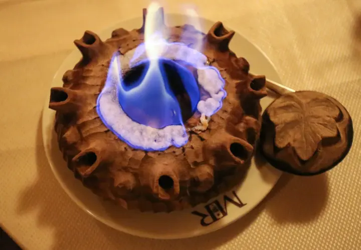 Caffè alla Valdostana in fiamme, servito in una coppa di terracotta con un coperchio intagliato.
